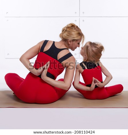Mother and daughter doing yoga exercise, fitness, gym wearing the same comfortable tracksuits, family sports, sports paired siting back on relax pose and holding hand back they are on red skinny suit