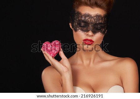 Young beautiful sexy woman with dark lace on eyes bare shoulders and neck, holding cake shape of heart to enjoy the taste and are dieting, feeling temptation, teeth passion sex red lips