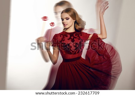 Beautiful sexy young woman with wavy blond hair and soft natural make-up in evening gown of chiffon and silk embroidered, holding a candy on a stick in the form of candy lips