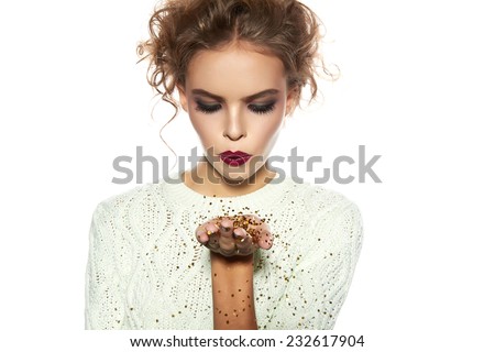 Beautiful sexy young blond girl with wavy hair bright evening make-up red lips long fluffy eyelashes holds palm with gold sequins in front of him and blows them a holiday New Year Christmas joy fun