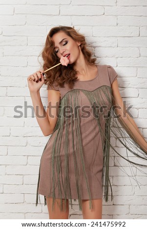 Beautiful young sexy girl with long wavy blond hair with evening make-up perfect summer tan thin figure in a short evening cocktail dress clothes for meeting shoes on a background of white brick wall