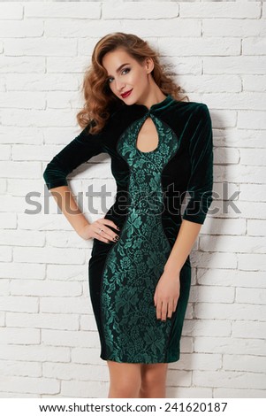 Beautiful young sexy girl with long wavy blond hair with evening makeup perfect summer tan thin figure in a short evening cocktail dress clothes for meeting shoes on a background of white brick wall