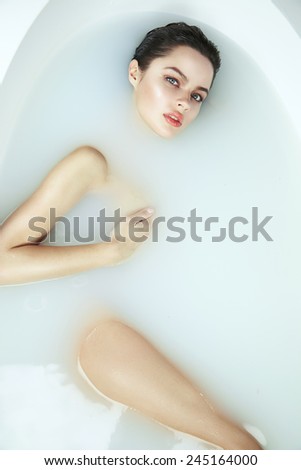 Beautiful young sexy girl with dark hair wet, evening makeup, taking bath with milk or paraffin tan perfect skin in romantic atmosphere, beauty cosmetic salon and spa for woman at Valentine\'s Day