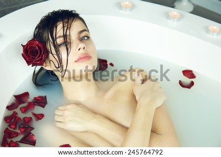 Beautiful young sexy woman with dark hair wet, evening makeup, takes bath with milk and rose petals and candles, beauty salon and spa Valentine