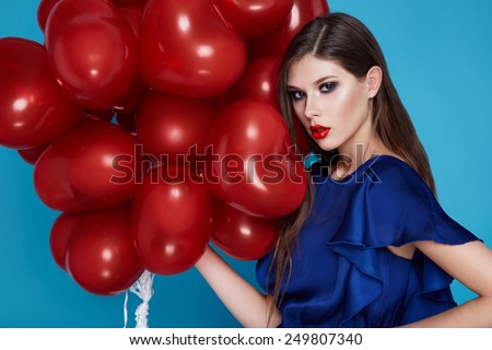 Beautiful young sexy girl with long hair brunette woman with evening make-up cosmetics dressed in a blue silk dress dekzhit in hand many red balloons party Valentine\'s Day heart and love