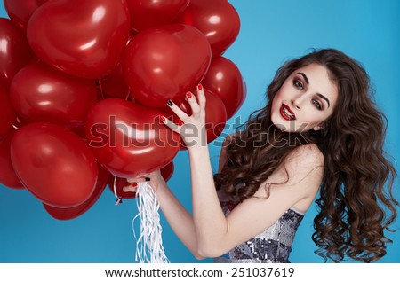 Beautiful young sexy girl with long hair brunette woman with evening make-up cosmetics dressed in a silver dress holding in hand many red balloons party Valentine\'s Day heart and love