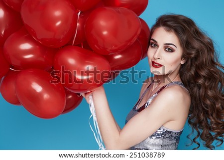Beautiful young sexy girl with long hair brunette woman with evening make-up cosmetics dressed in a silver dress holding in hand many red balloons party Valentine\'s Day heart and love