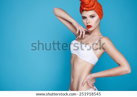 Beautiful young sexy girl with bright makeup perfect slim figure trained body and tan diet fitness club wearing a white stylish trendy top and orange headscarf sport underwear