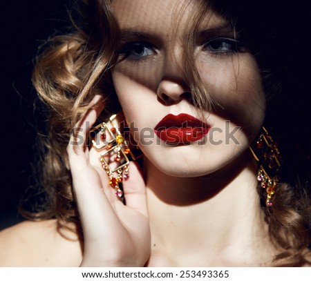Closeup of the face belong to beautiful young sexy blonde girl with curly hair pure snow white skin and bright makeup red lips, red lipstick, long earrings in dark shadows of palm leaves