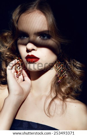 Closeup of the face belong to beautiful young sexy blonde girl with curly hair pure snow white skin and bright makeup red lips, red lipstick, long earrings in dark shadows of palm leaves