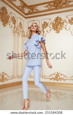 Beautiful sexy young blonde girl with long thick wavy hair thin slender figure perfect body and pretty face make-up wearing a light blue suit delicate high heels