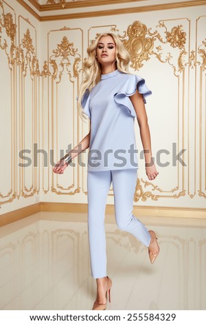 Beautiful sexy young blonde girl with long thick wavy hair thin slender figure perfect body and pretty face make-up wearing a light blue suit delicate high heels