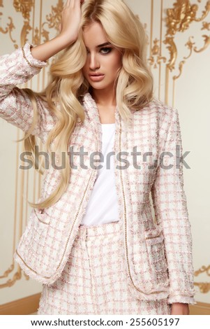 Beautiful sexy young blonde girl with long thick wavy hair thin slender figure perfect body and pretty face make-up wearing a light pink suit delicate high heels