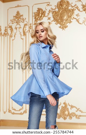 Beautiful sexy young blonde girl with long thick wavy hair thin slender figure perfect body and pretty face make-up wearing a light blue suit delicate and denim high heels