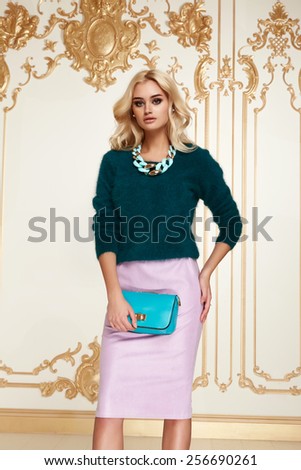 Beautiful sexy young blonde girl with long thick wavy hair thin slender figure perfect body and pretty face make-up wearing pink skirt green sweater small bag high heels