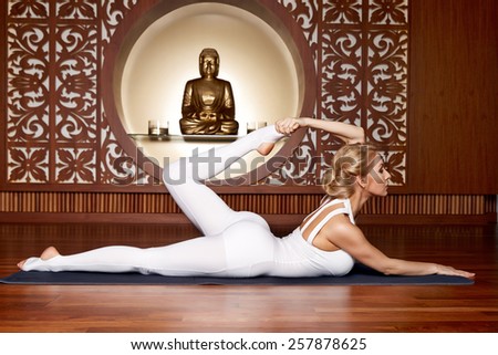 Beautiful young sexy blond girl with a sporty physique slender figure doing yoga exercises  fitness in slinky suit meditates relaxes pilates