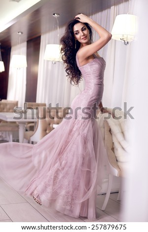 Beautiful sexy young brunette woman with long wavy hair thin slender figure perfect body and pretty face make-up wearing a purple evening skinny dress and jewelry