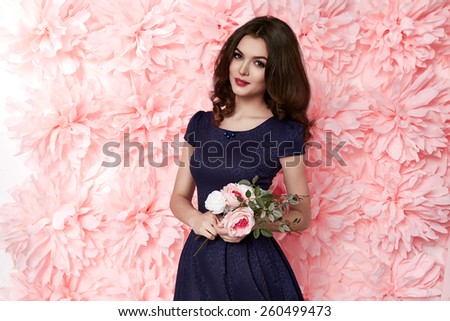 Beautiful young sexy girl with long wavy brunette hair with a bright evening make-up perfect summer tan thin figure dressed in colored short dress holding flower pink
