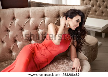 Beautiful sexy young brunette woman with long wavy hair thin slender figure perfect body and pretty face make-up wearing a red evening skinny dress and jewelry