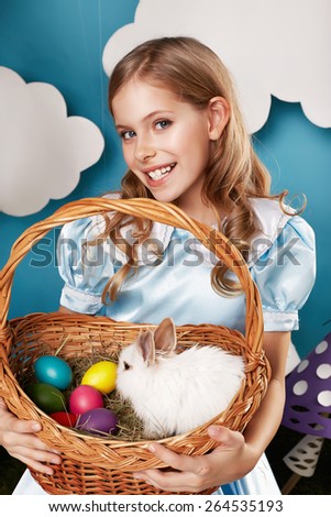 Little fluffy white Easter bunny sitting in a wicker basket on a background of blue sky and white clouds small beautiful cute  blonde girl holding