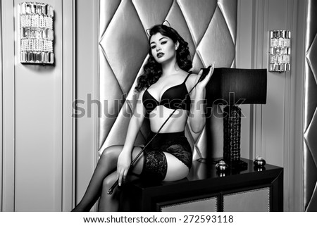 Beautiful sexy tanned brunette woman with  in black lace lingerie with a beautiful evening makeup sitting on the table next to wall hand strap with shoulder red lips perfect body