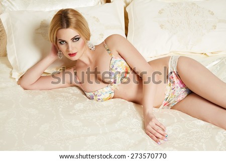 Beautiful sexy long-haired blonde woman sitting on a bed with pillows in lace lingerie silk linens flower evening makeup perfect body shape