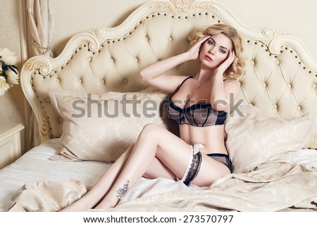 Beautiful sexy long-haired blonde woman sitting on a bed with pillows in lace lingerie silk linens flower evening makeup perfect body shape