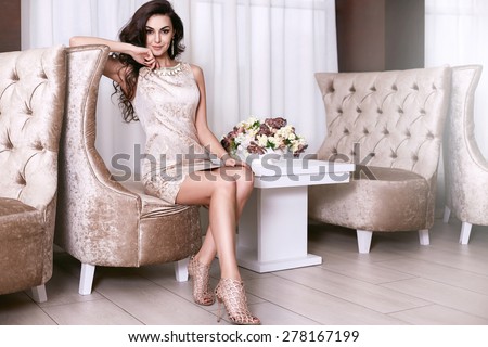 Beautiful sexy young brunette woman with long wavy hair thin slender figure perfect body and pretty face make-up wearing a beige evening skinny dress and jewelry