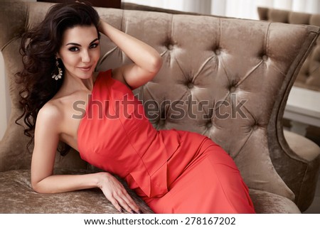 Beautiful sexy young brunette woman with long wavy hair thin slender figure perfect body and pretty face make-up wearing a red evening skinny dress and jewelry