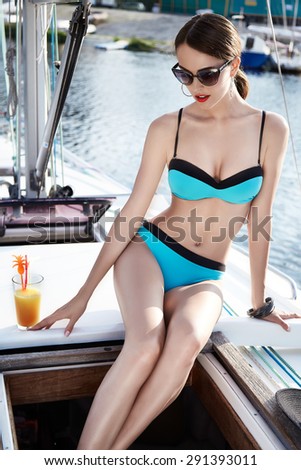 Beautiful brunette girl in good shape with long dark hair and tan skin red lips in fashion swimming suite hat in yacht beach river ocean with green water smile summer hot tan party cocktail sunglasses