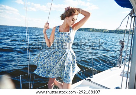 Beautiful young sexy brunette girl in a dress and makeup, summer trip on a yacht with white sails on the sea or ocean in the Gulf marine of the wind and the breeze in the sun tans romantic