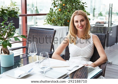 Beautiful young sexy blonde woman with make-up in a restaurant cafÃ?Â© or bar, breakfast or supper came to the party of business meetings, negotiations, dating, dressed in a trendy, designer white dress