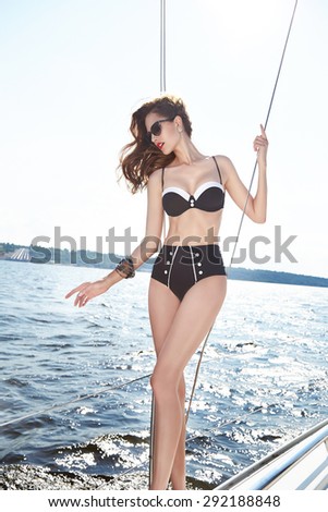 Beautiful brunette girl in good shape with long dark hair and tan skin red lips in fashion swimming suite hat  in yacht beach river ocean green water smile summer hot tan party cocktail hat sunglasses