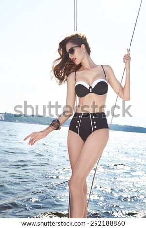 Beautiful brunette girl in good shape with long dark hair and tan skin red lips in fashion swimming suite hat  in yacht beach river ocean green water smile summer hot tan party cocktail hat sunglasses