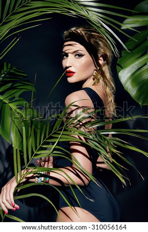 Beautiful young sexy young woman model with perfect figure and tanned skin body bright makeup oil and water drops on the hand wearing lots of bracelet palm leaves in the jungle shadows shining sun