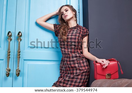 Beautiful fashionable stylish woman dressed in sexy short dress made natural fabrics bordeaux collection long hair makeup, fashion, style, interior gray room blue door holding a leather bag accessory
