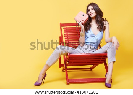 Glamour sexy girl clothes blue color silk blouse with lace beige cotton pants sit on chair  relax break hold trend bag stylish shoes beautiful face long brunette hair fashion collection model pose