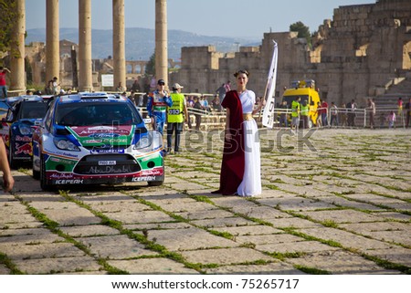 JERASH, JORDAN - APRIL 14: Female model dressed in ancient Roman costume stands next to a race car and she will escort racers to start platform of the Jordan Rally 2011 on April 14, 2011 in Jerash, Jordan.