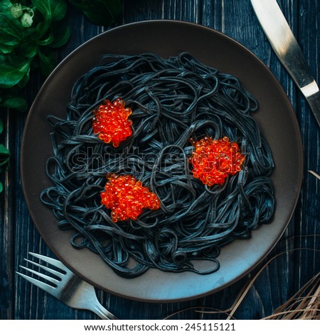 Black spaghetti with red caviar on a dark wooden table.