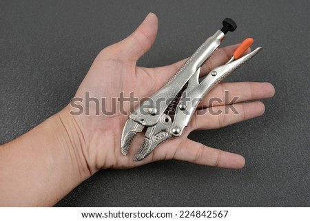 Locking pliers in hand man on black steel background