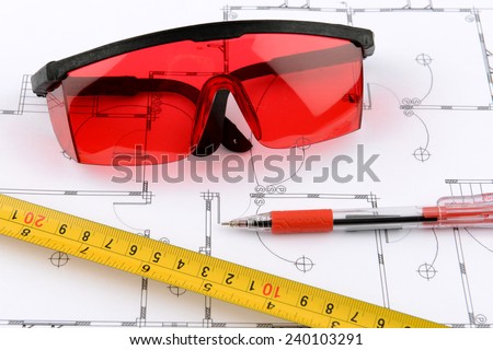 photo red protective spectacles and red pen and measuring tape on plans