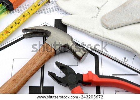 measuring tape, hammer, pliers, gloves and water level on plans