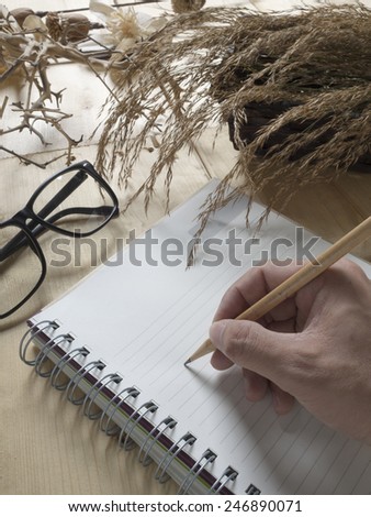 Vintage tone, Dry flowers, note, glasses, and pencil in hand on wood background
