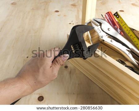 Wrenches in hand and wood toolbox on wood background