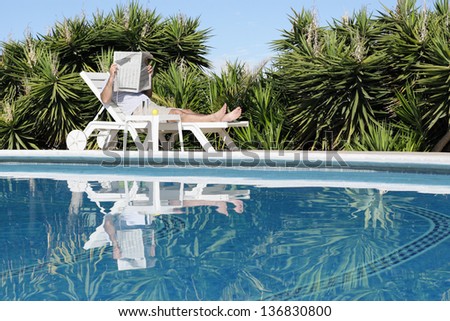 Man relaxing at the pool and  reading newspaper