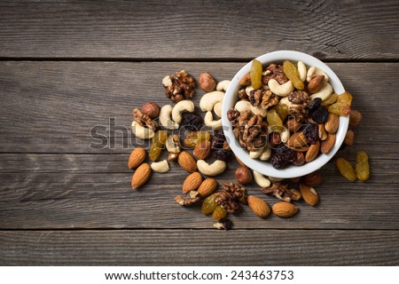 Assorted nuts in white bowl on wooden surface.