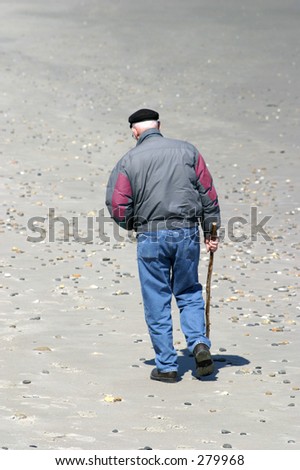 Elderly man walking alone on beach.