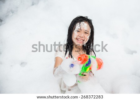 Little asian girl smiling and holding squirt gun in foam party