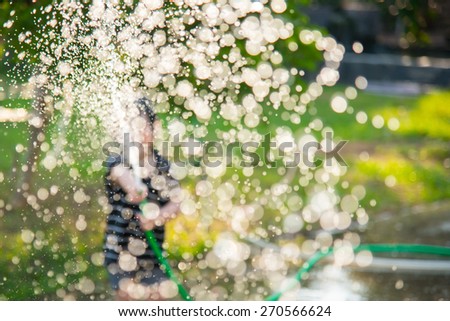 Blur background of Asian child playing with water hose outdoors in the garden at the backyard of the house on a hot sunny summer day