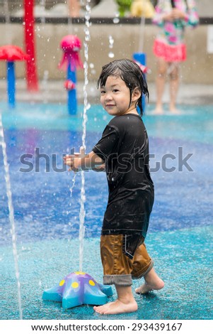 Happy asian boy has fun playing in water fountains in water park